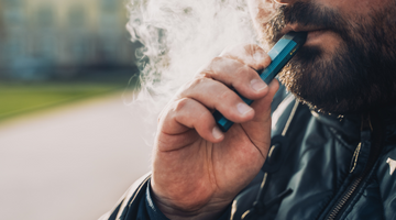 A man with a beard smoking a blue vape pen.